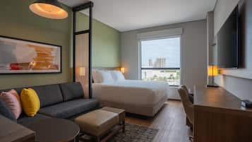 Una habitación de hotel moderna con cama, sofá, escritorio y un amplio ventanal con vista a la ciudad.