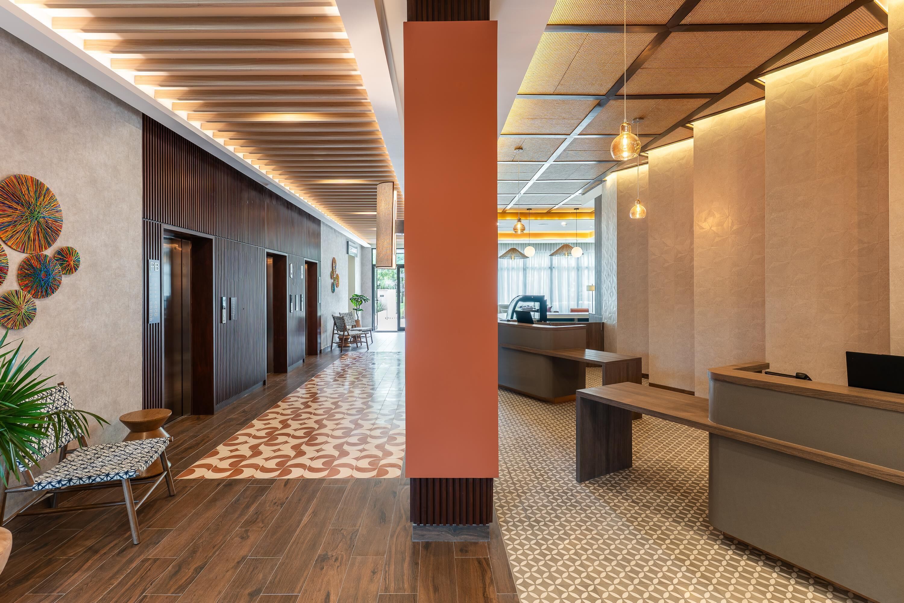 A modern hotel lobby with a wooden floor, a reception desk, and a seating area.