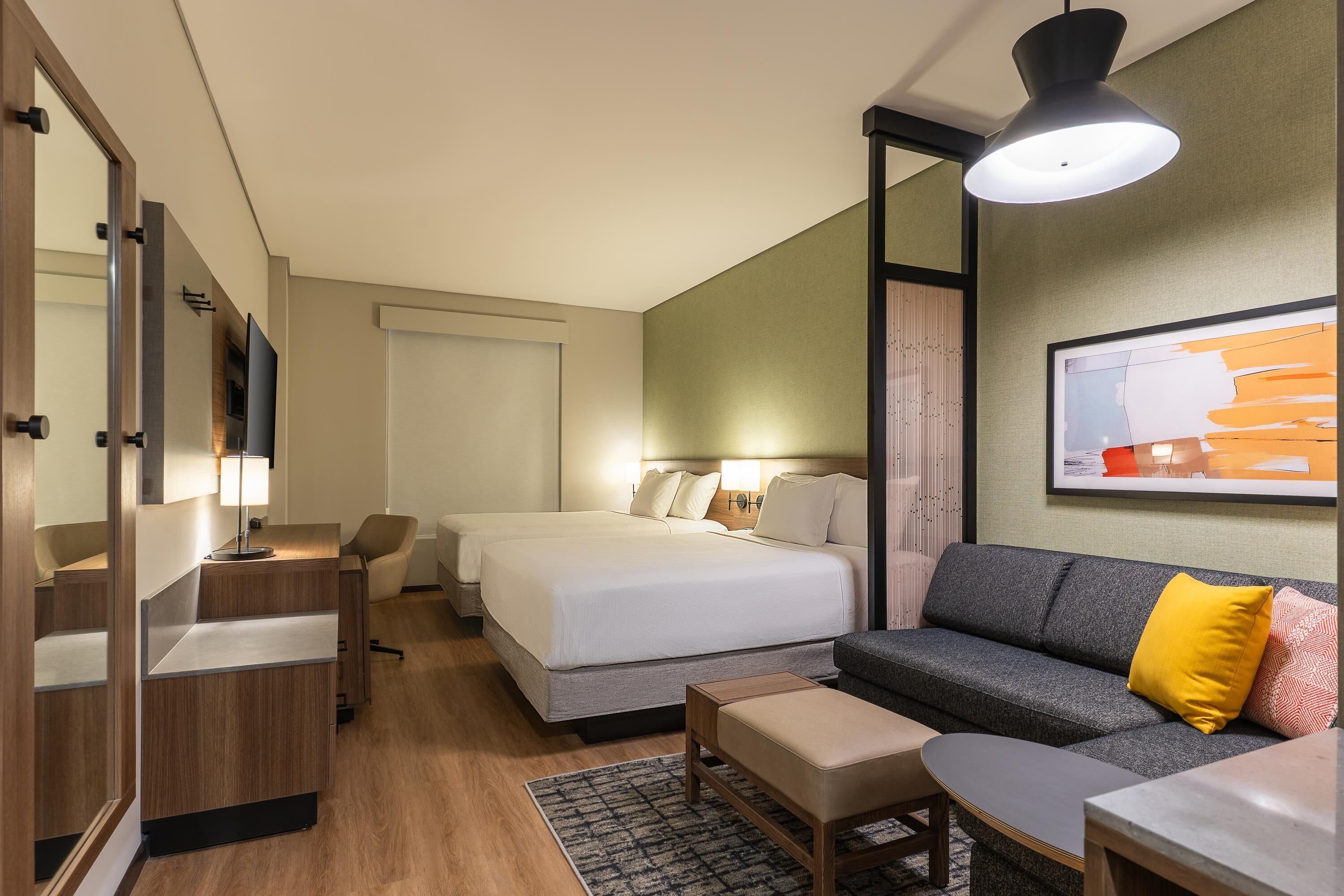 Habitación de hotel con cama, sofá, escritorio, silla, televisor y un cuadro en la pared.