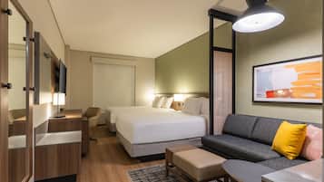 Habitación de hotel con cama, sofá, escritorio, silla, televisor y un cuadro en la pared.