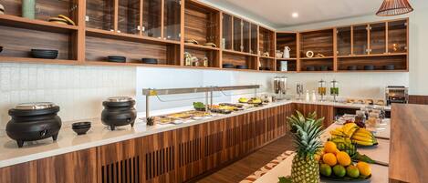 Une cuisine moderne avec des meubles en bois, un long comptoir et un présentoir à fruits.