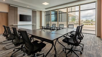 Une salle de conférence équipée d’une grande table, de six chaises, d’un téléviseur à écran plat et de grandes fenêtres donnant sur l’extérieur.