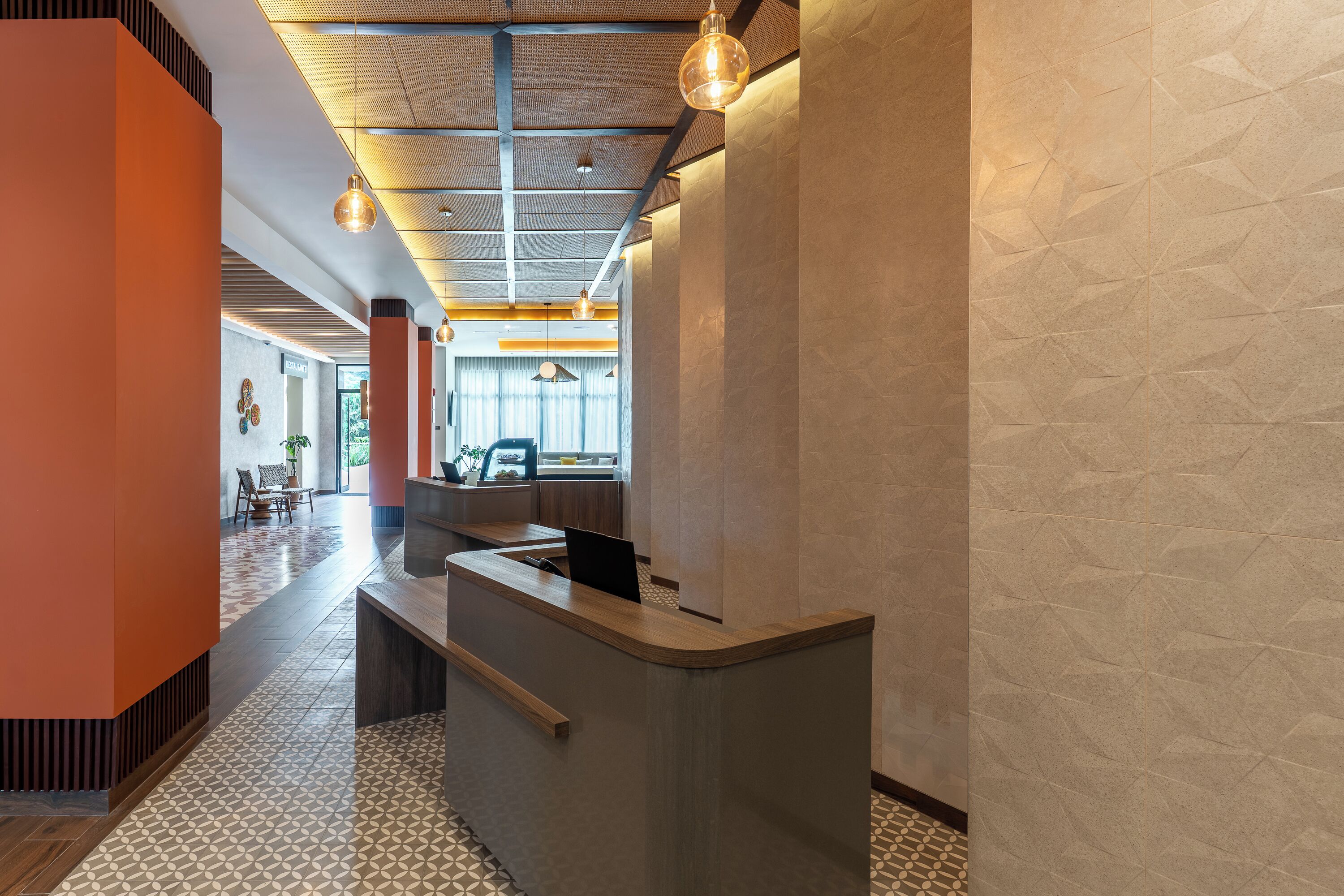 A reception area with a modern design, featuring a reception desk, patterned floor tiles, and a ceiling with exposed beams and hanging lights.