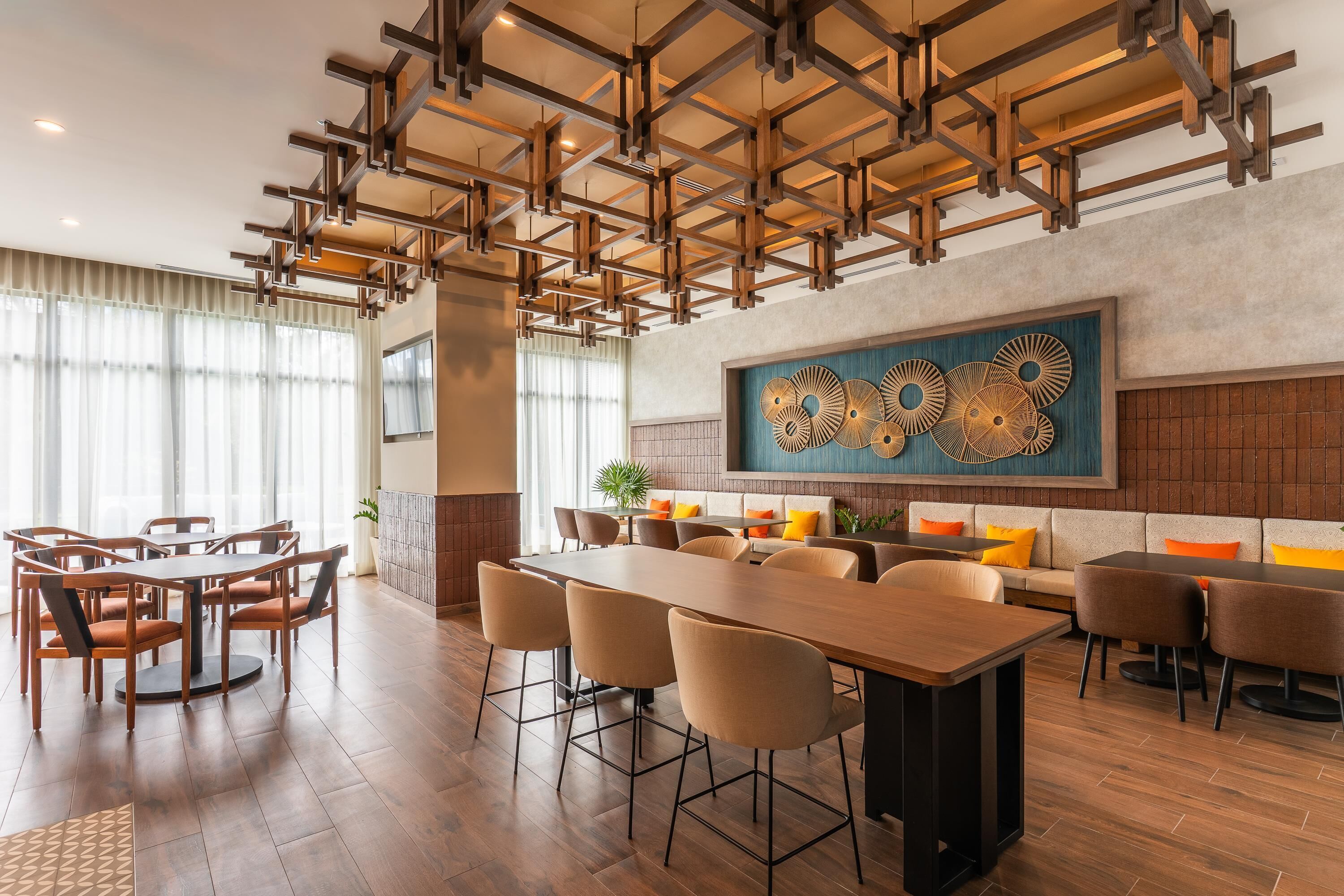 Un comedor moderno con una larga mesa de madera y sillas, un techo alto con vigas a la vista, y una gran obra de arte abstracto en la pared.