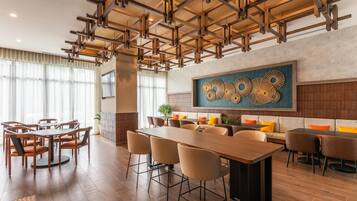 Un comedor moderno con una larga mesa de madera y sillas, un techo alto con vigas a la vista, y una gran obra de arte abstracto en la pared.