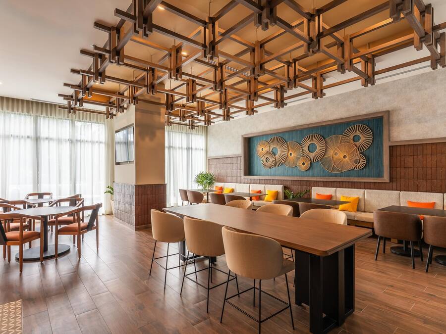 Un comedor moderno con una larga mesa de madera y sillas, un techo alto con vigas a la vista, y una gran obra de arte abstracto en la pared.