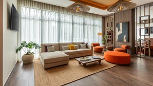 A modern living room with a sofa, ottoman, and coffee table, a large window with curtains, and a TV mounted on the wall. - Hyatt Place Merida/Via Montejo (Mérida)