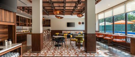 A modern restaurant with a central seating area, wooden accents, and large windows offering a view of the outdoors.