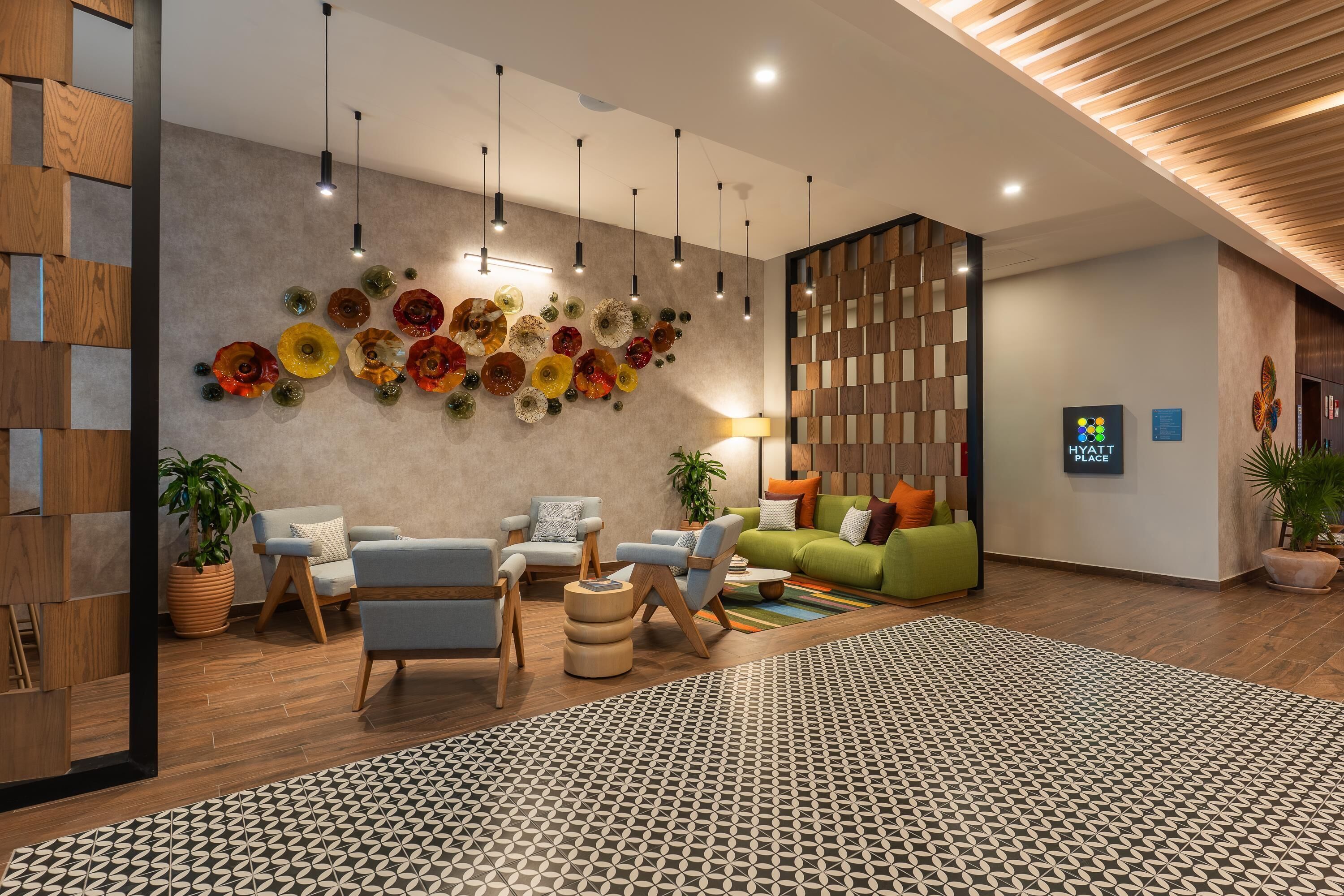 A modern lobby with a geometric patterned rug, a wall of colorful glass art, and contemporary furniture.