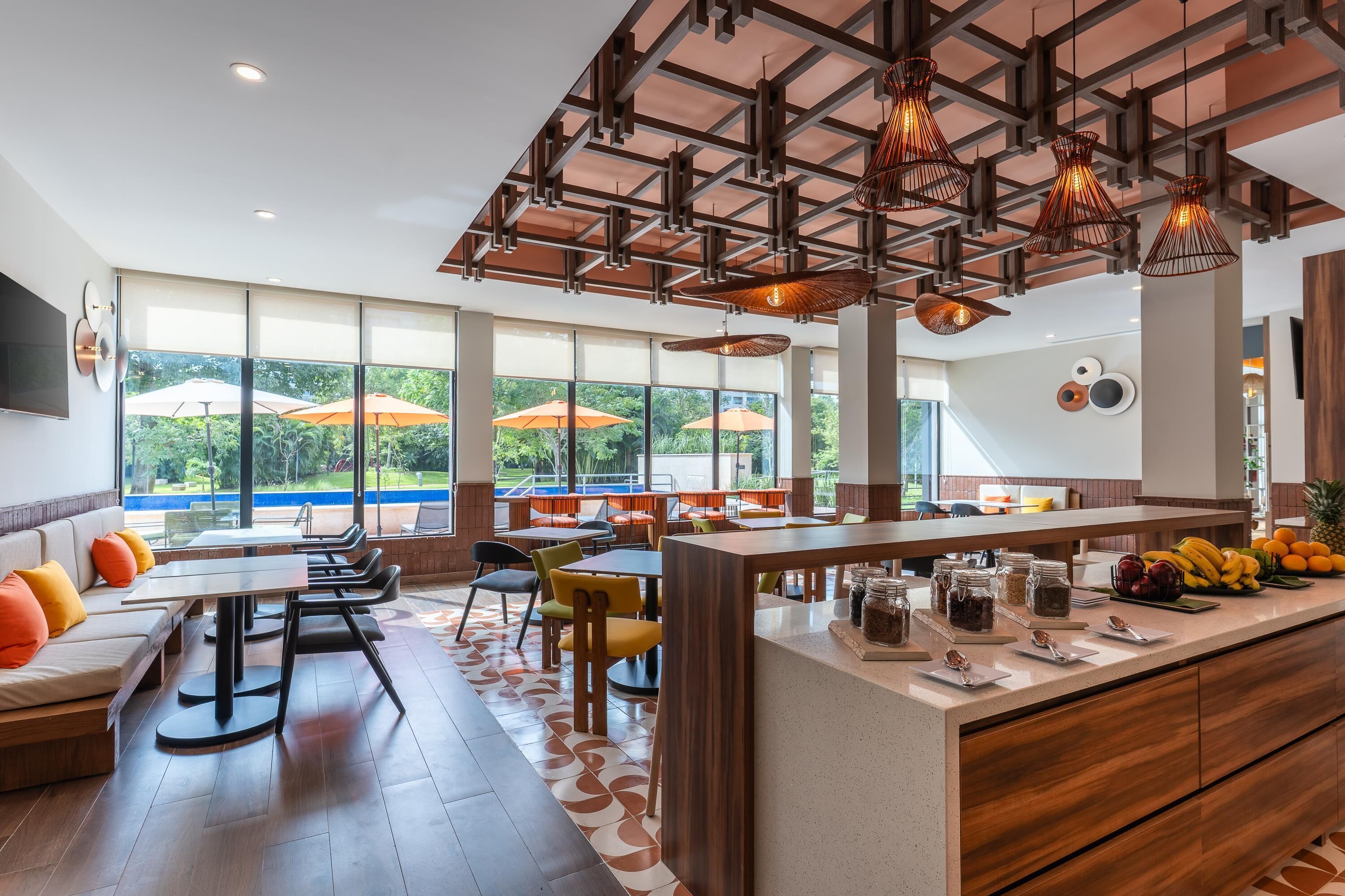 A modern restaurant with a long counter, multiple tables, and chairs. There are large windows with umbrellas outside.