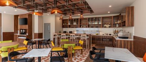 Un restaurante moderno con techos altos, vigas de madera y una zona central de comedor con mesas y sillas.