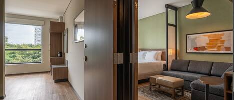 A modern hotel room with a large window, a sofa, a bed, and a small table.