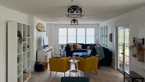 Un salon spacieux avec un canapé, des fauteuils jaunes, un téléviseur et une bibliothèque.