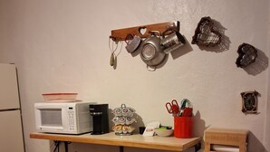 A compact kitchen with a microwave, kettle, and tea kettle on a shelf, a small trash bin, and a bookshelf with books. - Studio apt in the heart of town. (Lake City)