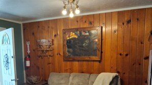 A cozy living room with a wooden-paneled wall, a gray sofa, a painting, and a dog paw print rug. - Studio apt in the heart of town. (Lake City)