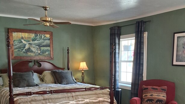 A bedroom with a four-poster bed, a red armchair, a forest-themed rug, and a painting of a bear on the wall. - Studio apt in the heart of town. (Lake City)