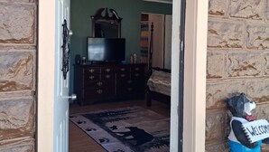An open doorway leading to a room with a wooden floor, a dresser, a television, and a bear statue with a 'WELCOME' sign. - Studio apt in the heart of town. (Lake City)