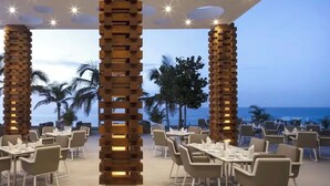 Un restaurante con terraza, pilares de madera y vista al océano.