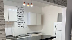 A modern kitchen with a black countertop, white cabinets, and a stone backsplash. There are two black bar stools and a white refrigerator.