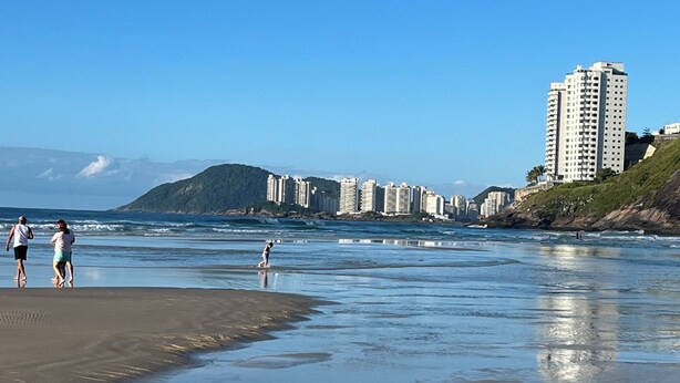 A beach with people walking, a sandy shore, and buildings in the background.