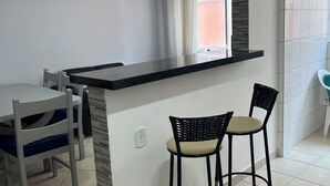 A kitchen with a black countertop, two bar stools, a ceiling fan, and a window with curtains.