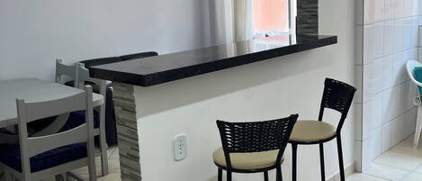 A kitchen with a black countertop, two bar stools, a ceiling fan, and a window with curtains.