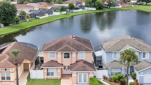 Zona residencial con casas, un lago y un coche blanco estacionado en la entrada.