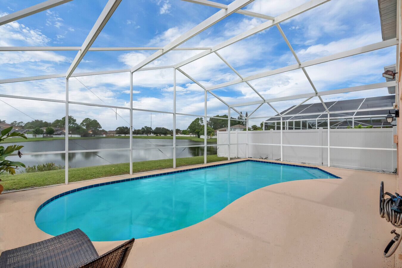 Una piscina exterior cubierta con vista a un lago, rodeada por una valla blanca y una casa al fondo.