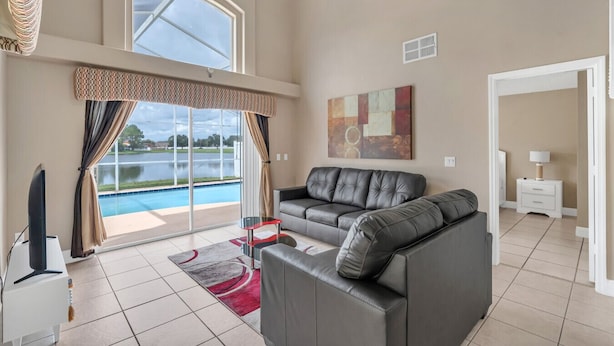 Un salón amplio con un sofá de cuero gris, un televisor de pantalla plana y un ventanal con vistas a una piscina.