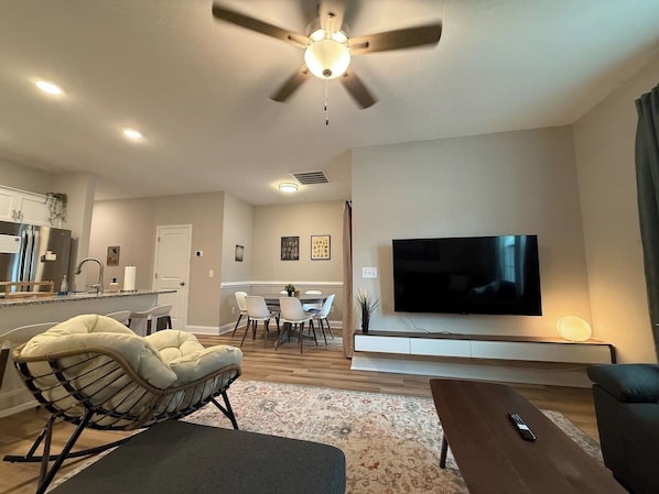 A modern living room with a flat-screen TV, a ceiling fan, and a dining area with chairs and a table.