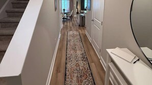 Un couloir avec un tapis, un escalier et une porte donnant sur une autre pièce.
