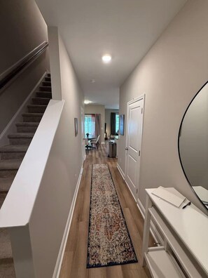 A hallway with a carpet, a staircase, and a door leading to another room.