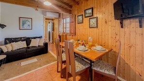 Un intérieur en bois avec une table à manger dressée pour deux personnes, un canapé et un téléviseur fixé au mur.
