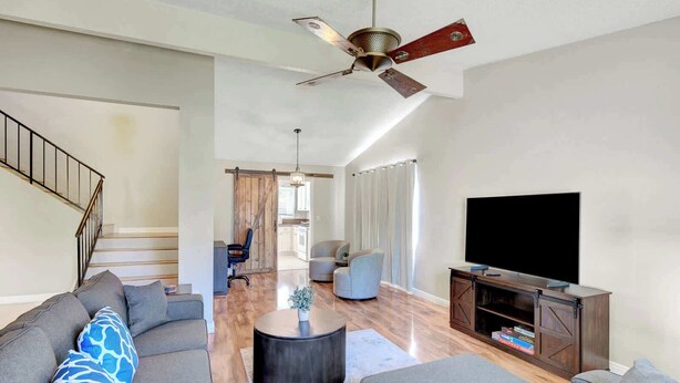 Ein geräumiges Wohnzimmer mit einer großen Couch, einem Couchtisch, einem TV-Schrank und einem Deckenventilator.