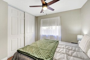 A bedroom with a bed, a ceiling fan, a window with sheer curtains, and a nightstand with a lamp. - A- ZLV HOME 2 (Henderson)