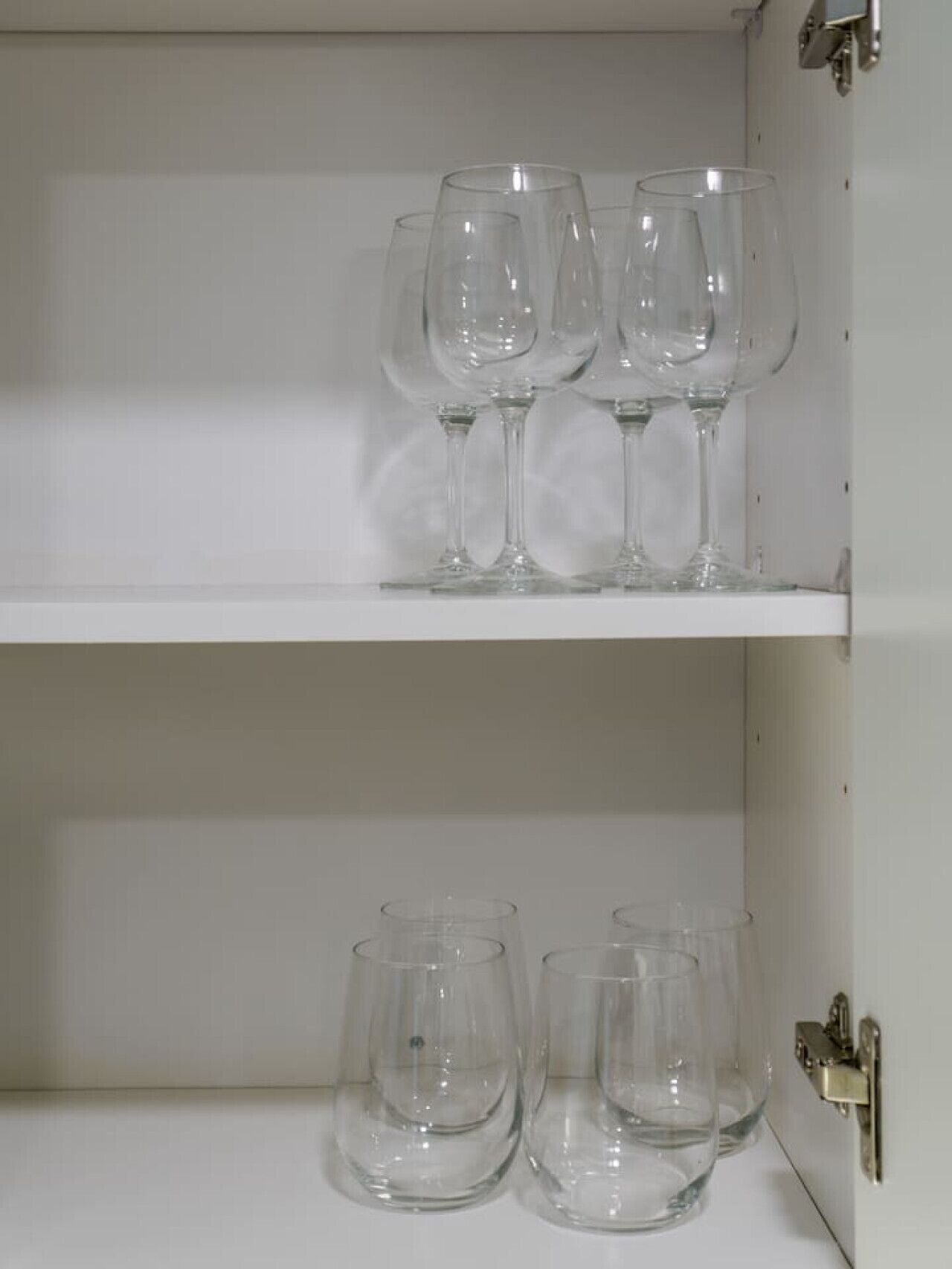 Ein weißes Schränkchen mit zwei Einlegeböden, auf denen klares Glasgeschirr steht.