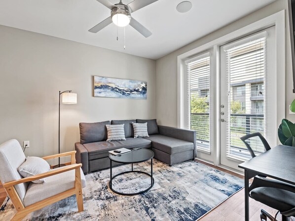 A modern living room with a gray sectional sofa, a round coffee table, a wooden armchair, and a dining table. - Comfy King bed | Pool + Gym + Parking + Stockyards (Fort Worth)