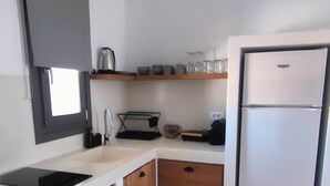 A compact kitchen with a built-in sink, wooden cabinets, a stainless steel refrigerator, and a window above the sink.
