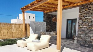 A modern outdoor lounge area with two wooden loungers, a stone wall, and a covered pergola.