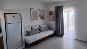 A modern living room with a sofa, a flat-screen TV, a refrigerator, and a window with curtains.