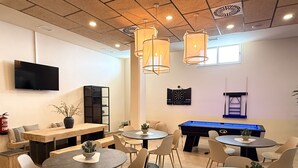 Un área de lounge moderna con varias opciones de asientos, incluyendo mesas redondas y sofás, una mesa de billar y un dardo.
