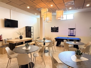 Un espace de détente moderne offrant de nombreuses options d’assises, notamment des tables rondes et des canapés, ainsi qu’une table de billard et un jeu de fléchettes.