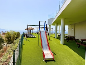 Un terrain de jeux équipé d’un toboggan, de balançoires et de tables de pique-nique, offrant une vue panoramique.