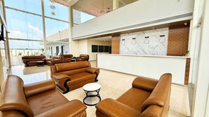 A spacious lobby with leather sofas, a reception desk, and a large window offering a view of the outdoors. - The Grand Omkara Hotel & Resorts (Khandwa)