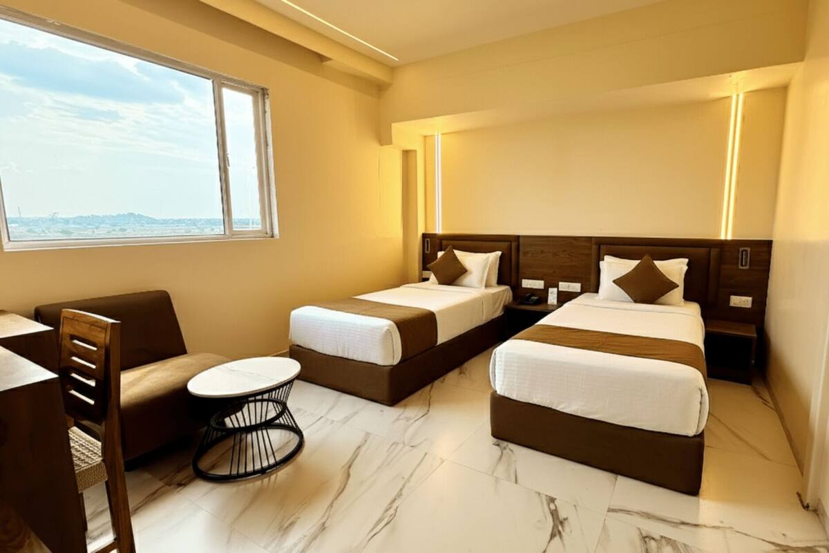 A hotel room with two single beds, a sofa, a small round table, and a large window offering a view.