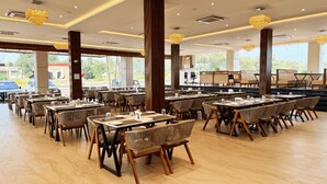 A spacious restaurant with multiple tables and chairs, large windows, and decorative chandeliers. - The Grand Omkara Hotel & Resorts (Khandwa)