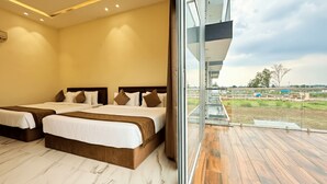 A hotel room with two beds, a balcony with a view of the countryside, and a large window. - The Grand Omkara Hotel & Resorts (Khandwa)