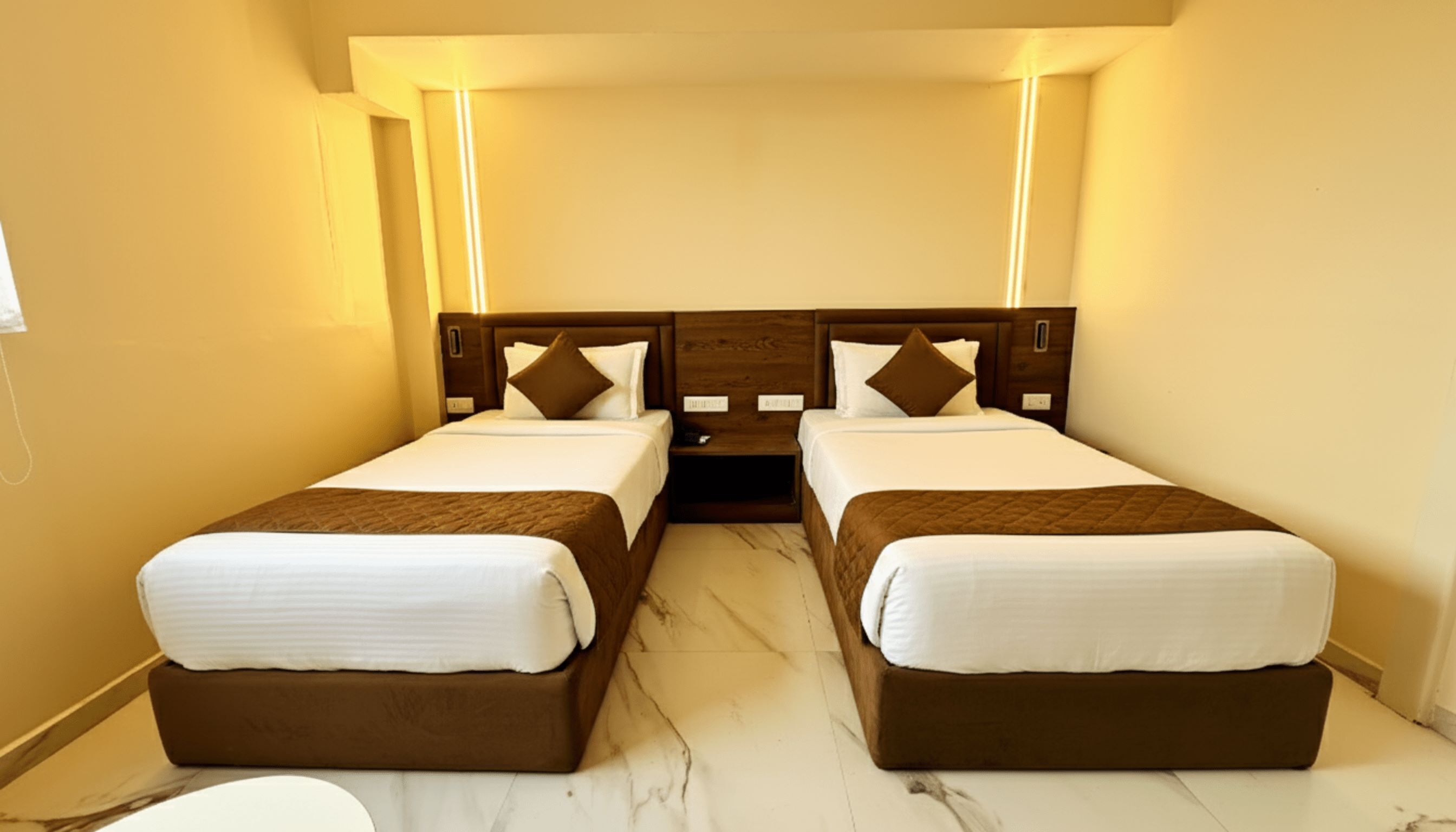 Une chambre d’hôtel avec deux lits, une tête de lit en bois, du linge de lit blanc et un sol en marbre.