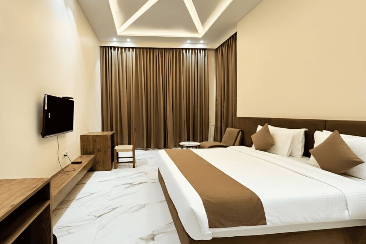 A hotel room with a large bed, a desk, a chair, a TV, and a curtain backdrop.