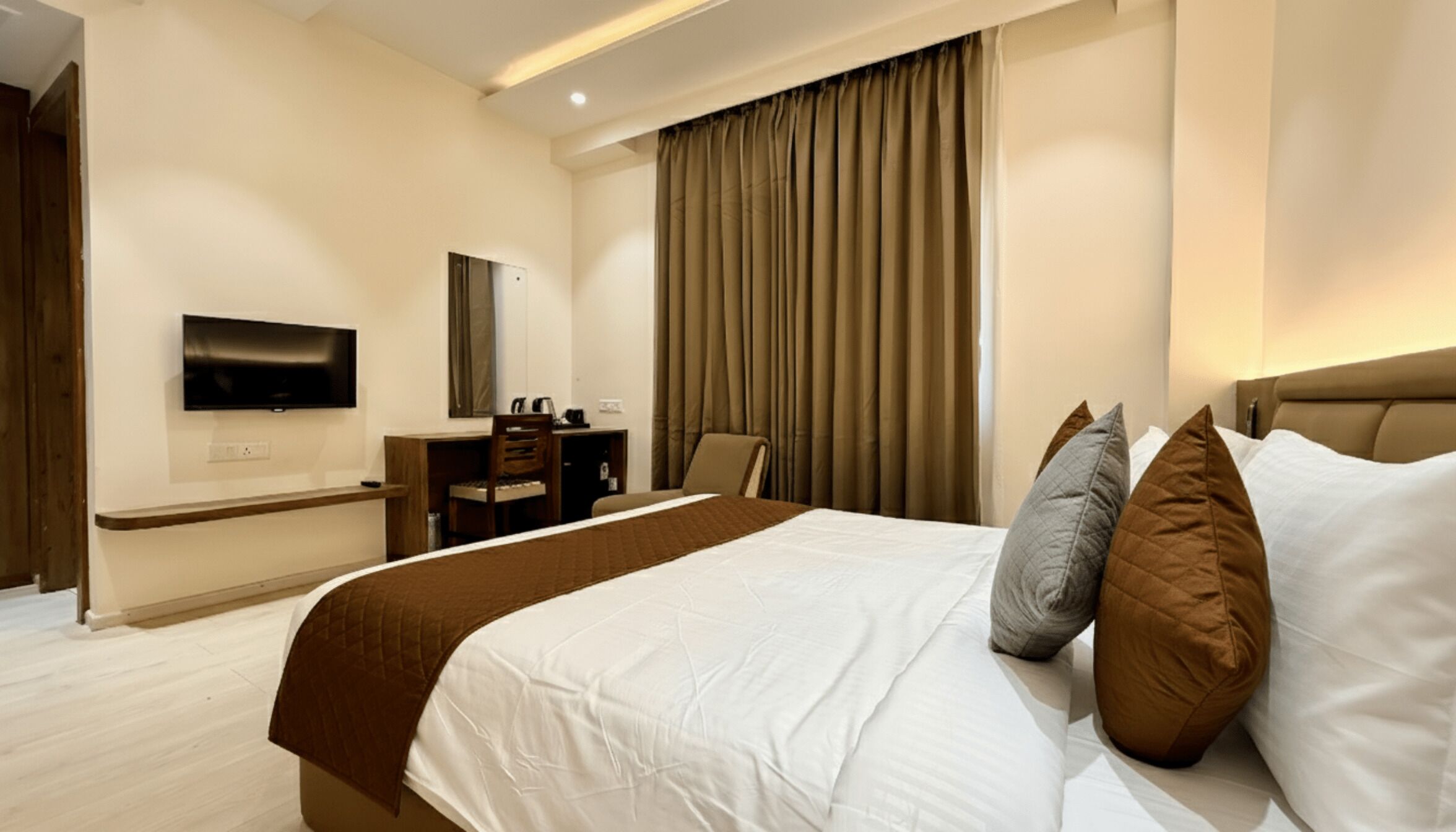 A hotel room with a large bed, a desk, a chair, a television, and a window with curtains.